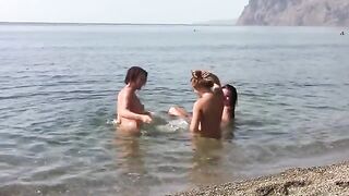 Three naked girls on the beach with a crest each to cover themselves