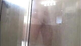 A guy washes his body under the shower with a camera