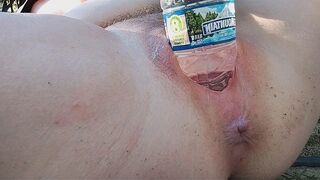 A sexy brunette reaches intense pleasure while masturbating outdoors with a water bottle